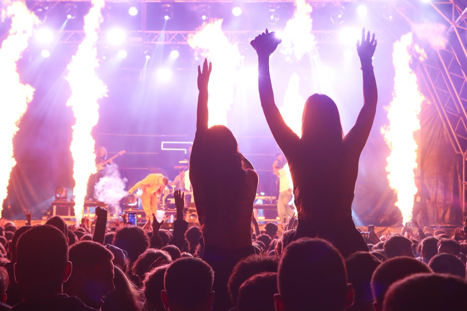 A concert crowd lit by pyrotechnics and fire on stage